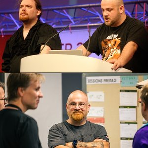 Das Bild zeigt zwei Personen, die an einem Podium stehen und etwas präsentieren. Die Umgebung sieht wie ein Veranstaltungsort oder eine Konferenz aus. Die Männer tragen legere, aber stilvollere Kleidung, was auf eine eher informelle Atmosphäre hindeutet. Insgesamt vermittelt das Bild den Eindruck einer Präsentation oder eines Vortrags vor einem Publikum.