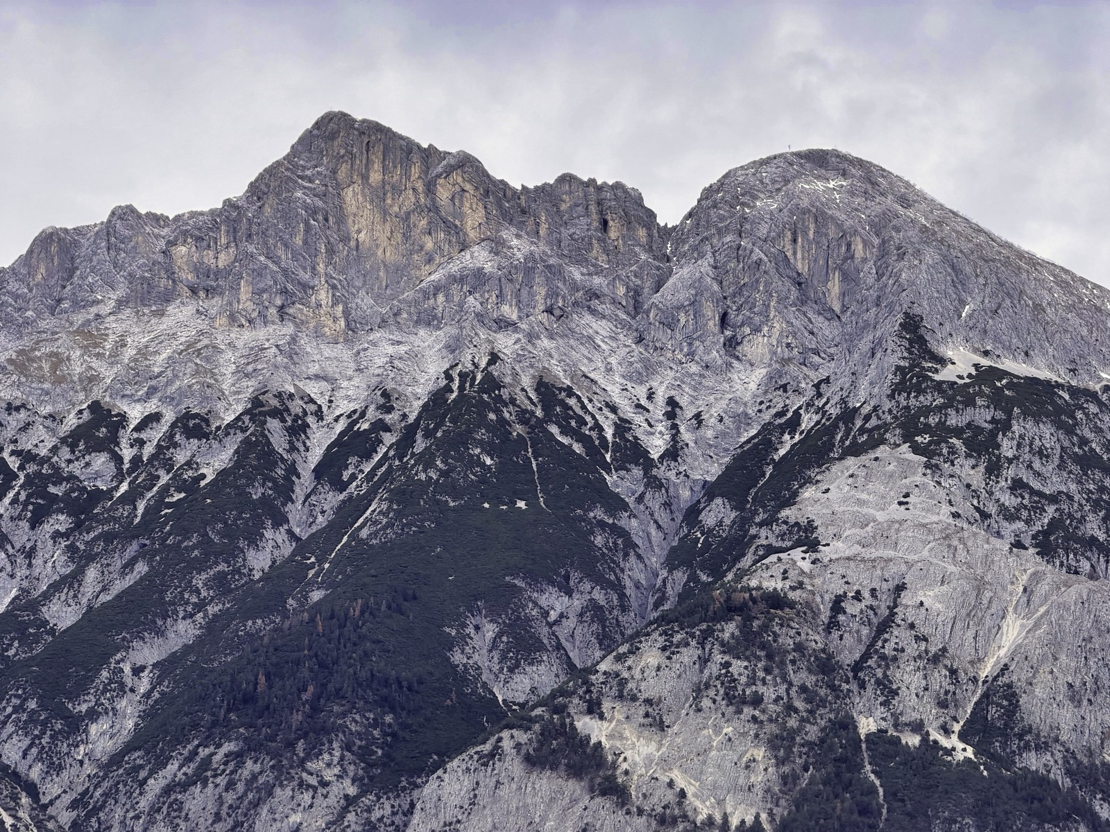Das Bild zeigt eine beeindruckende Berglandschaft mit massiven, felsigen Gipfeln, die sich in einem kalten, grauen Licht abheben. Die steil aufragenden Felsen und Bergrücken vermitteln eine Stimmung von Majestät und Erhabenheit in dieser einsamen, unwirtlichen Umgebung. Die Szene ist geprägt von einer rauhen, aber faszinierenden Schönheit der Natur.