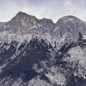 Das Bild zeigt eine beeindruckende Berglandschaft mit massiven, felsigen Gipfeln, die sich in einem kalten, grauen Licht abheben. Die steil aufragenden Felsen und Bergrücken vermitteln eine Stimmung von Majestät und Erhabenheit in dieser einsamen, unwirtlichen Umgebung. Die Szene ist geprägt von einer rauhen, aber faszinierenden Schönheit der Natur.