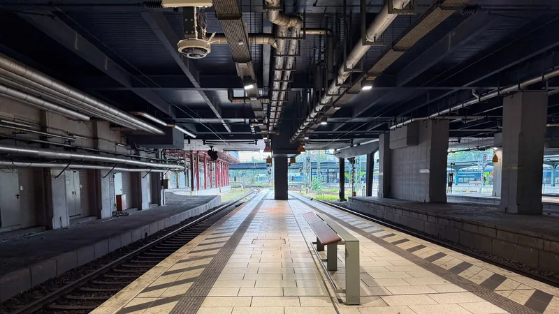 Das Bild zeigt einen großen, dunklen und weitläufigen Bahnhof. Die Decke ist mit Rohren und elektrischen Leitungen übersät, der Boden ist mit Fliesen ausgelegt. Insgesamt vermittelt das Bild eine eher kühle, industrielle Atmosphäre, die auf einen wichtigen Verkehrsknotenpunkt hindeutet.